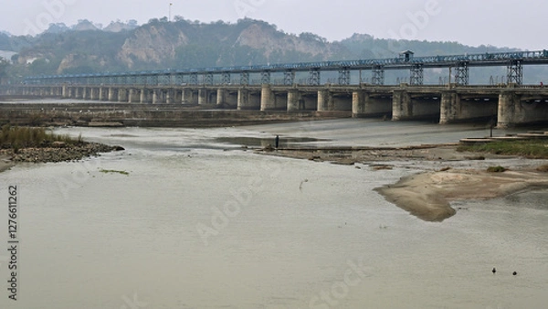 Fototapeta Long, multi-span bridge crossing a wide river with a low water level, exposing patches of sand and rocks.