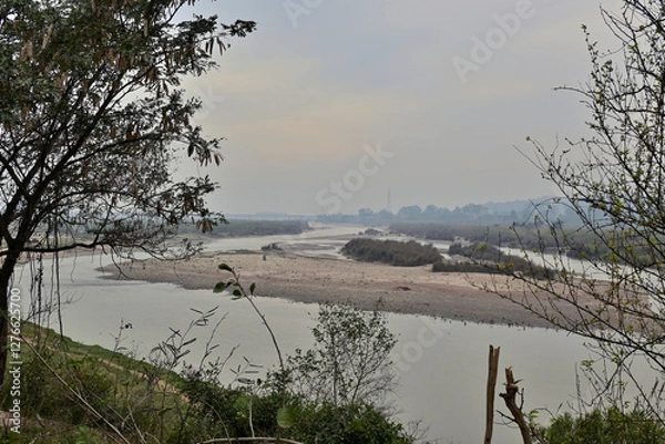 Fototapeta Serene river scene with a sandy shoreline winding into the distance.