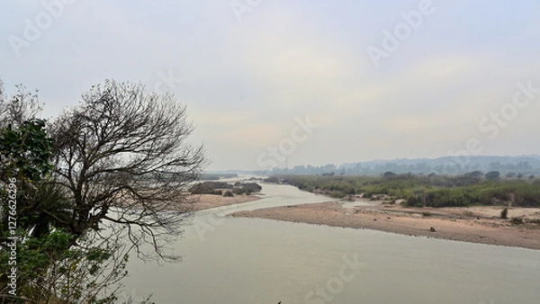 Fototapeta A serene landscape features a gently flowing river bordered by sandy banks.