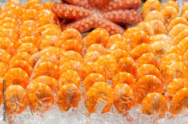 Fototapeta Fresh Shrimp with blurred Octopus background on Ice. A vibrant close-up of seafood of freshly cooked shrimp and octopus arranged on a bed of crushed ice.