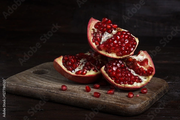 Obraz cut part of pomegranate on a wooden board on a wooden background.