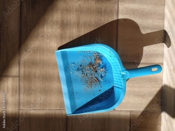 Obraz Blue plastic dustpan with household garbage on floor in sunlight