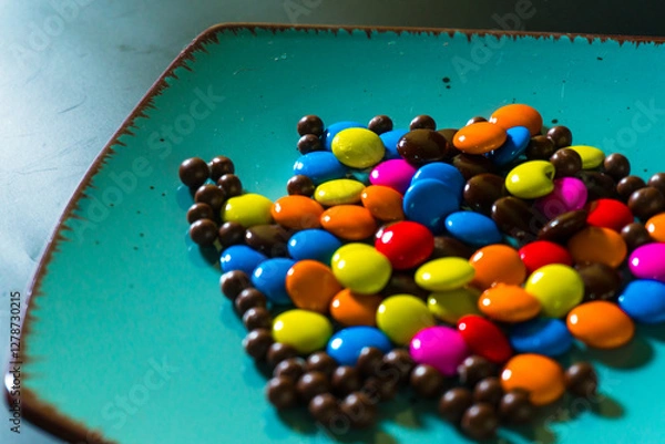 Fototapeta Close-up of colorful chocolate candies on a vibrant turquoise plate, perfect for food and confectionery themes