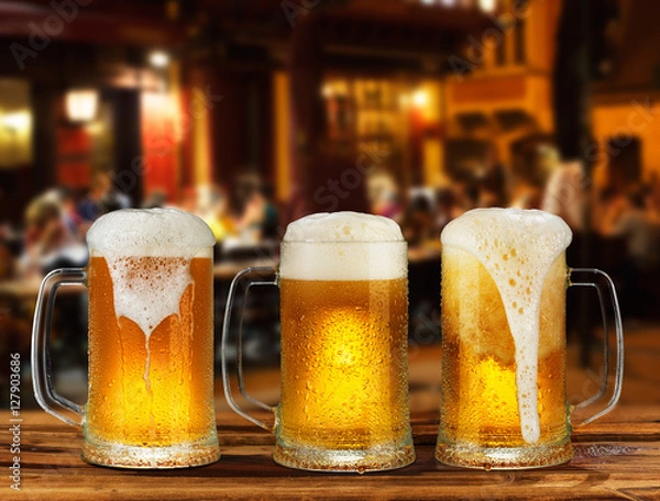 Fototapeta cold glass mug of beer with foam on the background of the street