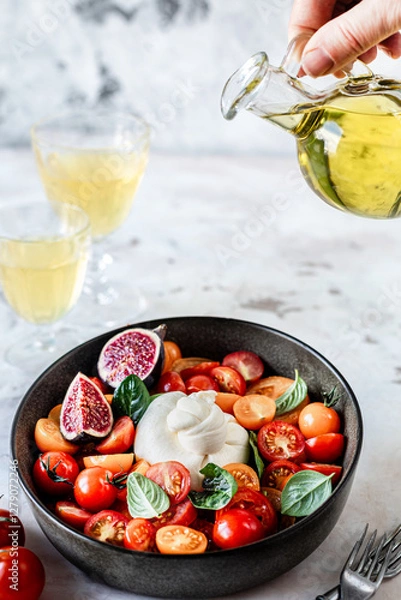 Fototapeta burrata ball with cherry tomatoes, basil leaves, figs and olive oil in a bowl on the table.