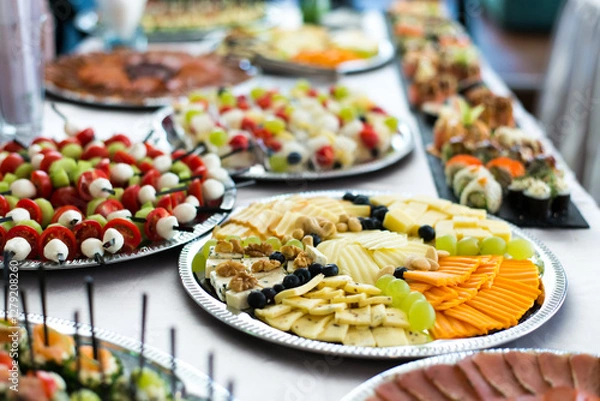 Fototapeta Snacks for the holiday, catering. Various snacks. Assortment of salads, sushi and buffet dishes. Meat, fish, cheese, salads, fruits and vegetables, sauces and canapes for celebrating a festive event.