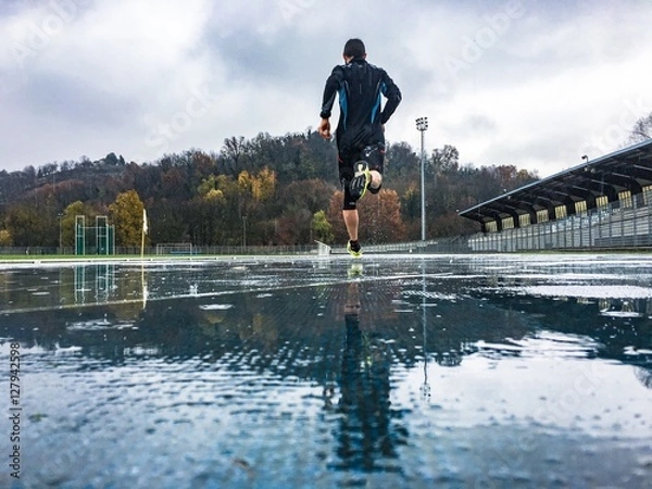 Fototapeta  Man running on athletic track in a rainy day