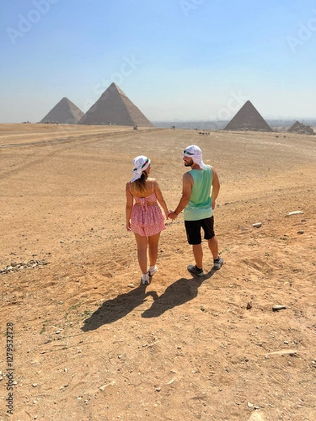 Fototapeta Couple walking hand in hand towards the Pyramids of Giza.
