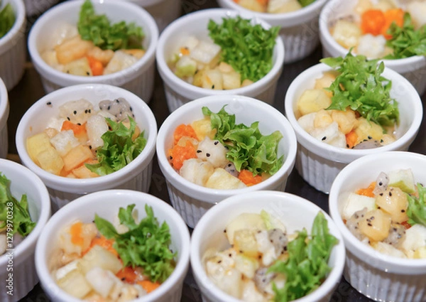 Fototapeta Fresh Fruit Salad in Arranged White Ramekins. The fruit salad includes diced tropical fruits such as dragon fruit, pineapple, papaya, melon, garnished with green lettuce and black sesame seeds.