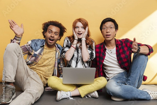 Fototapeta Three surprised young people sitting and using laptop
