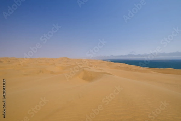 Fototapeta Endless golden dunes stretch towards the horizon, where the vast Namib Desert meets the Atlantic Ocean in the breathtaking wilderness of Sandwich Harbour, Namibia.