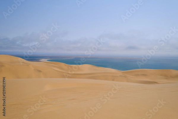 Obraz Sweeping sand dunes descend into the deep blue waters of the Atlantic, showcasing the stunning contrast of Namibia’s remote Sandwich Harbour, where the desert meets the sea.