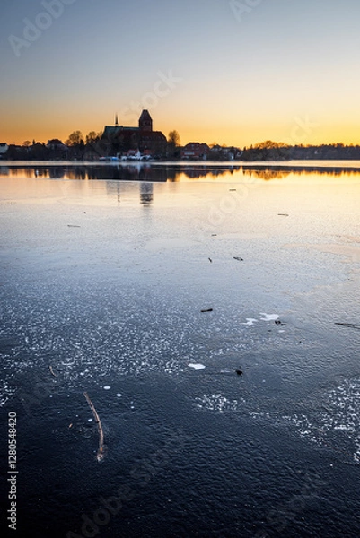 Fototapeta Dome of Ratzeburg in winter with colorful sunset with ice in foreground