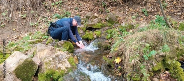 Fototapeta A man with a camera washes his hands in a stream near a spring on an autumn day