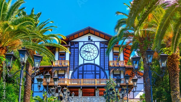 Obraz Beautiful view of the Gagripsh Restaurant against the background of green tropical palm trees and sun glare in Gagra, Abkhazia. Summer vacation, travel, relaxation of tourists in a tropical country.
