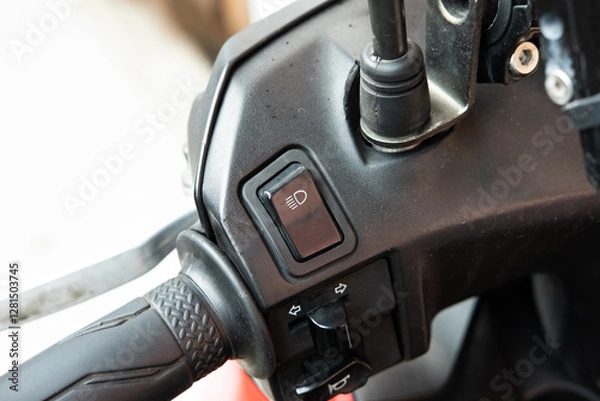 Fototapeta A close-up of a high-beam and low-beam headlight switch on a black scooter or motorcycle, highlighting its textured button and placement on the handlebar