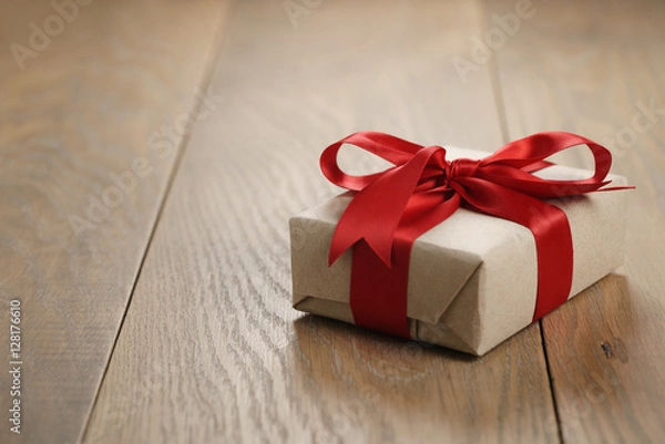 Fototapeta rustic craft paper gift box with red ribbon bow on wood table, shallow focus