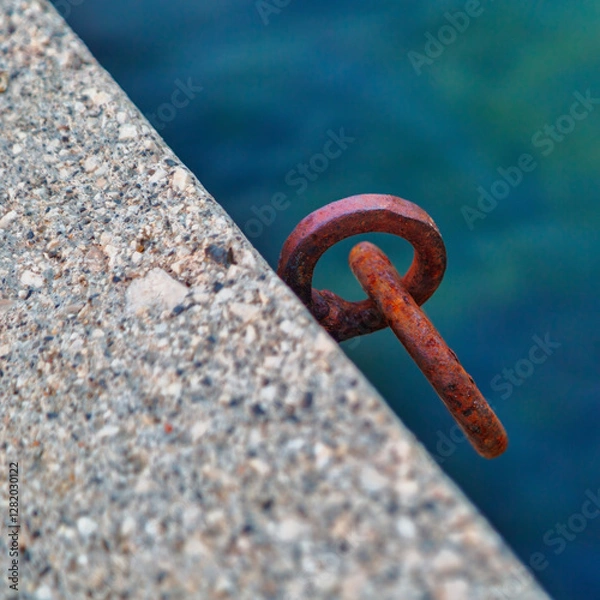 Fototapeta Rusty iron mooring ring for boat on concrete pier against sea water background