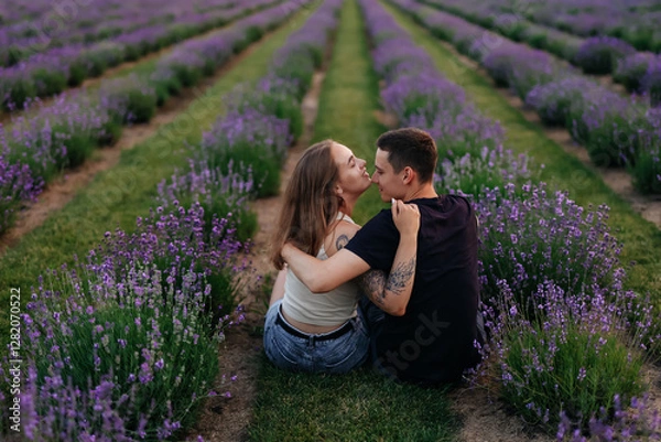 Fototapeta young couple in love man and girl on a walk on the street in nature under the open sky hugging and kissing. Lavender field with purple flowers for a romantic couple of people in love