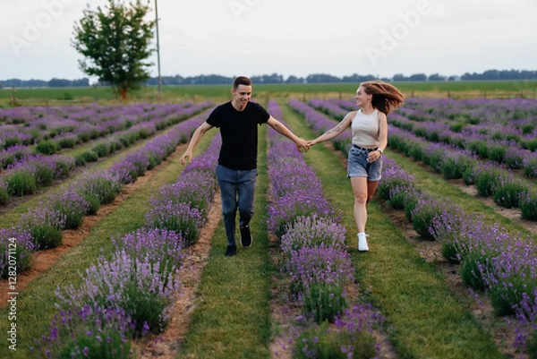 Fototapeta young couple in love man and girl on a walk on the street in nature under the open sky hugging and kissing. Lavender field with purple flowers for a romantic couple of people in love