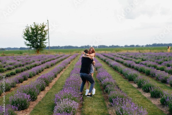 Fototapeta young couple in love man and girl on a walk on the street in nature under the open sky hugging and kissing. Lavender field with purple flowers for a romantic couple of people in love