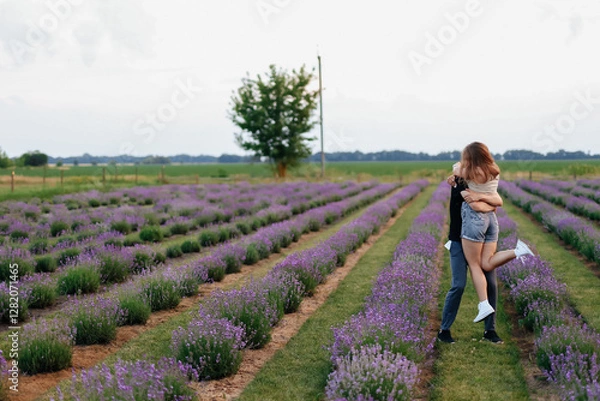Fototapeta young couple in love man and girl on a walk on the street in nature under the open sky hugging and kissing. Lavender field with purple flowers for a romantic couple of people in love