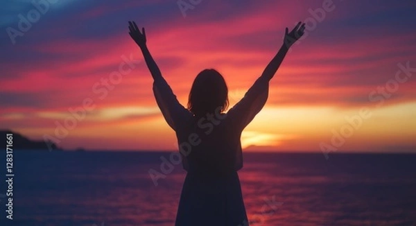 Fototapeta Silhouette of a woman with raised arms against a sunset sky over a sea background.