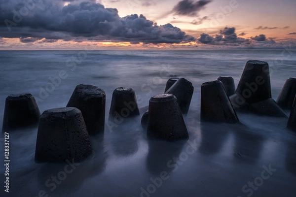 Obraz The sun is falling, silhouette of the concrete breakwaters are reflected on the smooth surface of the wet sand at the shore of Curonian spit 