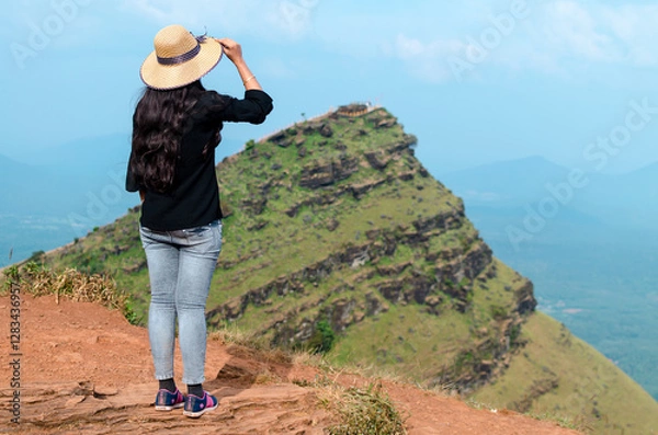 Fototapeta A female traveler  wearing a hat and posing by looking towards the view of Deviramma Betta in Chikkamagaluru, Karnataka, India