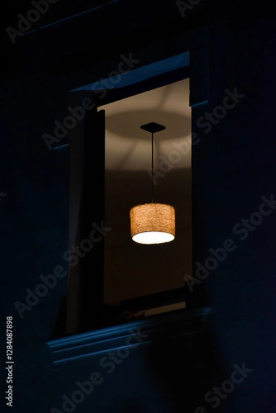 Fototapeta open window of an old house at night showing a dark environment with a chandelier lit in the center of the ceiling that reflects shadows