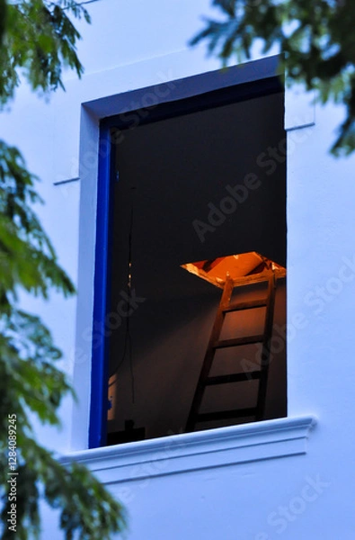 Fototapeta open window of an old house showing a dark environment with a ladder that goes up to the illuminated attic