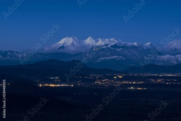 Obraz Snow-capped mountain at twilight. Soft glow of city lights in the valley below. A perfect winter landscape capturing the contrast between untouched alpine nature above and human activity below.