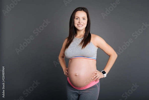 Fototapeta Happy pregnant sportswoman with hands around the waist