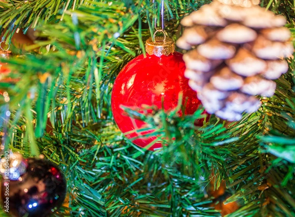 Fototapeta Red ornaments and pine cones on green artificial Christmas tree 