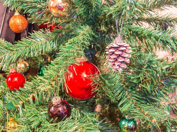 Fototapeta Red ornaments and pine cones on green artificial Christmas tree 