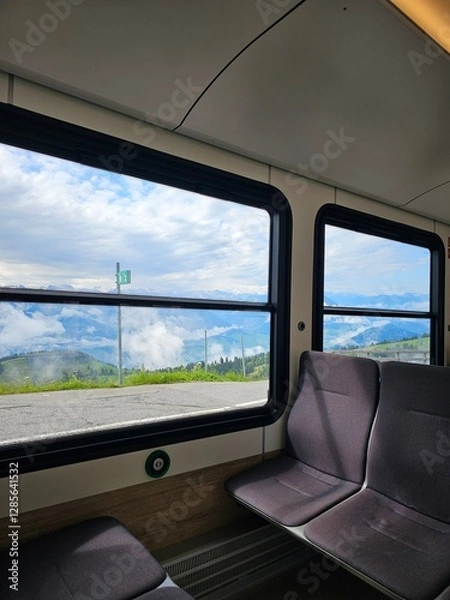 Fototapeta A unique and captivating photo taken inside a train on Mount Rigi, Switzerland, offering a scenic view of the stunning Swiss Alps. The image features the comfortable and cozy interior of the train, wi