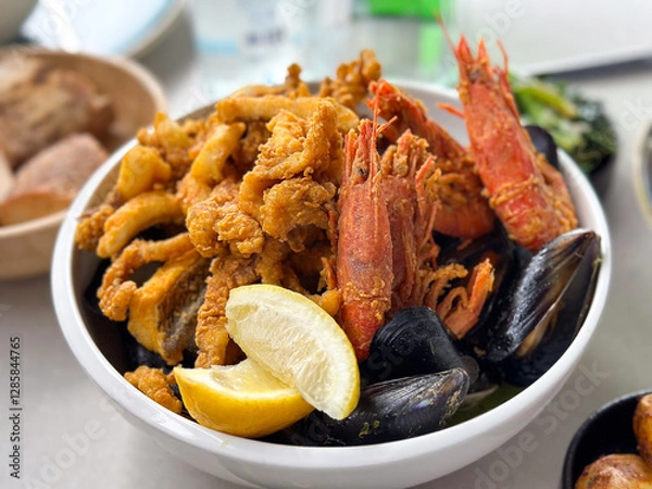 Fototapeta Seafood in a bowl with shrimps, shells, lemon and fried octopus with vegetables, potatoes and bread