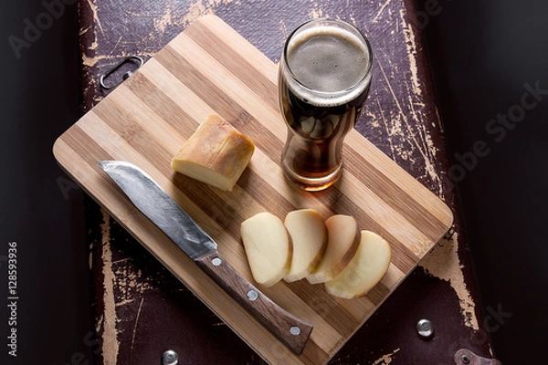 Obraz Glass with dark beer with smoked cheese on cutting board.