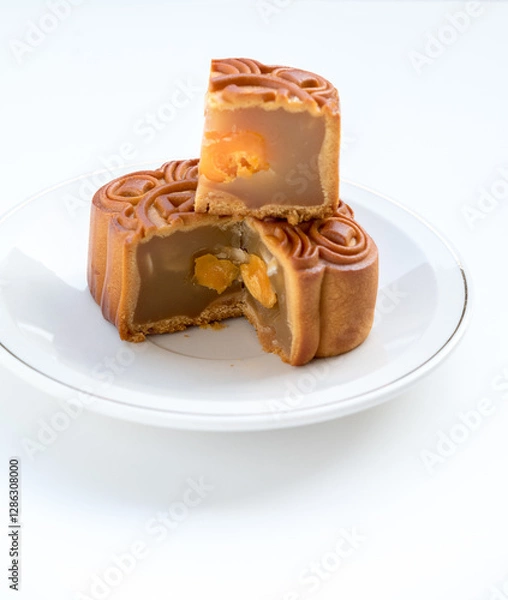 Fototapeta Mooncake with stacked slices showing filling and double egg yolks. Angled shot on a white plate. Bright lighting shows intricate details