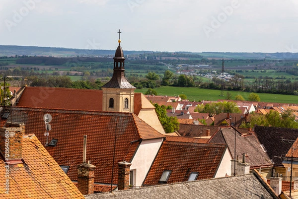 Obraz Scenic rooftop view of Mikulov with church tower and countryside. A picturesque view over the red-tiled rooftops of Mikulov, Czech Republic, featuring a historic church tower with rolling green fields