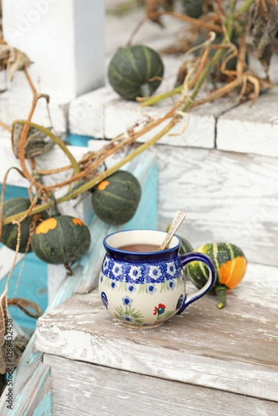 Obraz A beautiful ceramic tea cup on the stairs of the old veranda with small autumn pumpkins. Selective focus.
