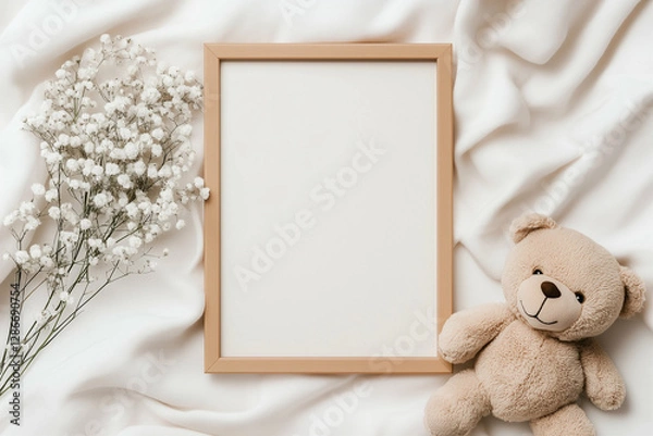 Obraz Teddy bear and photo frame with white flowers on white fabric. Teddy bear sitting next to a wooden frame and flowers on a white background. Top view of a teddy bear frame and flowers