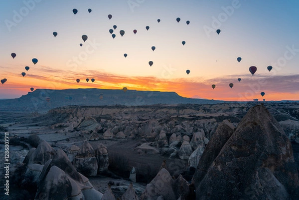 Fototapeta Aerial view of numerous hot air balloons floating above rock formations in Cappadocia, Turkey, in the morning light