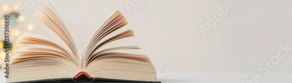 Fototapeta An open book rests on a surface, showcasing its pages, with a soft background that adds a warm, inviting ambiance.