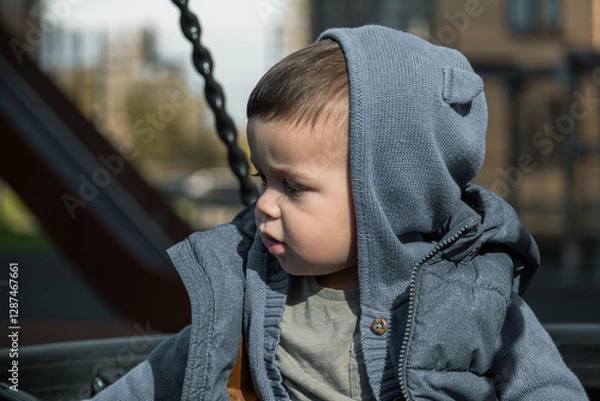 Fototapeta Portrait of a one-year-old child in the courtyard of residential buildings on a swing