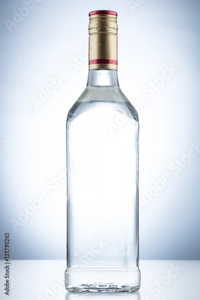 Fototapeta Empty tequila alcohol bottle with no label and a gold and red cap on a white background