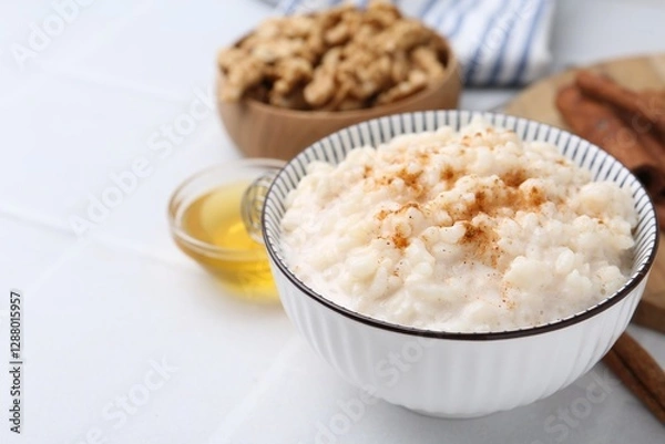 Fototapeta Tasty rice pudding with cinnamon served on white tiled table, closeup