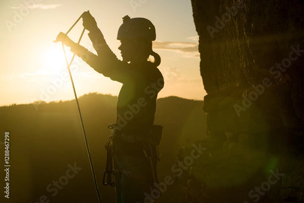 Fototapeta Young girl is preparing for training on the rocks sunset, in the mountains and puts a helmet on her head for safety to protect her health