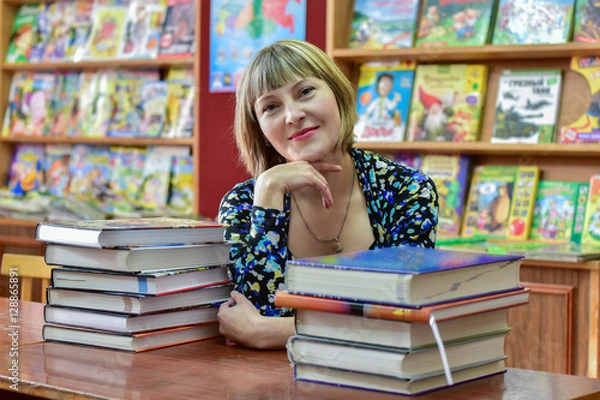 Obraz Information age/The girl - librarian talking on a smartphone on the background of bookshelves