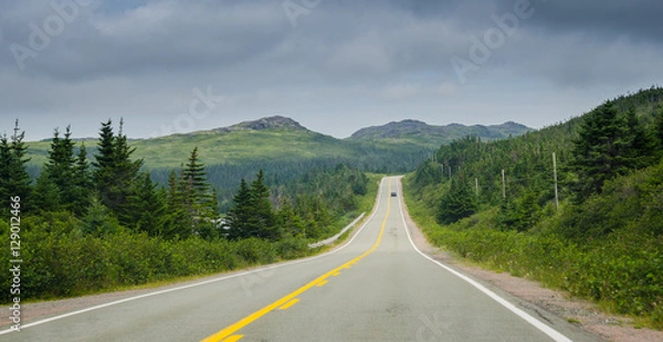 Fototapeta Newfoundland highway in overcast skies.  Lone car goes down the road.  Coastal highways in foothills and valley ranges of Newfoundland. 
